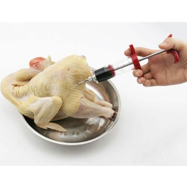 BBQ marinade injector syringe in use on raw chicken in a bowl