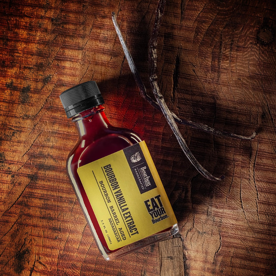 Bourbon-barrel vanilla extract bottle on wooden barrel with amber liquid, black cap