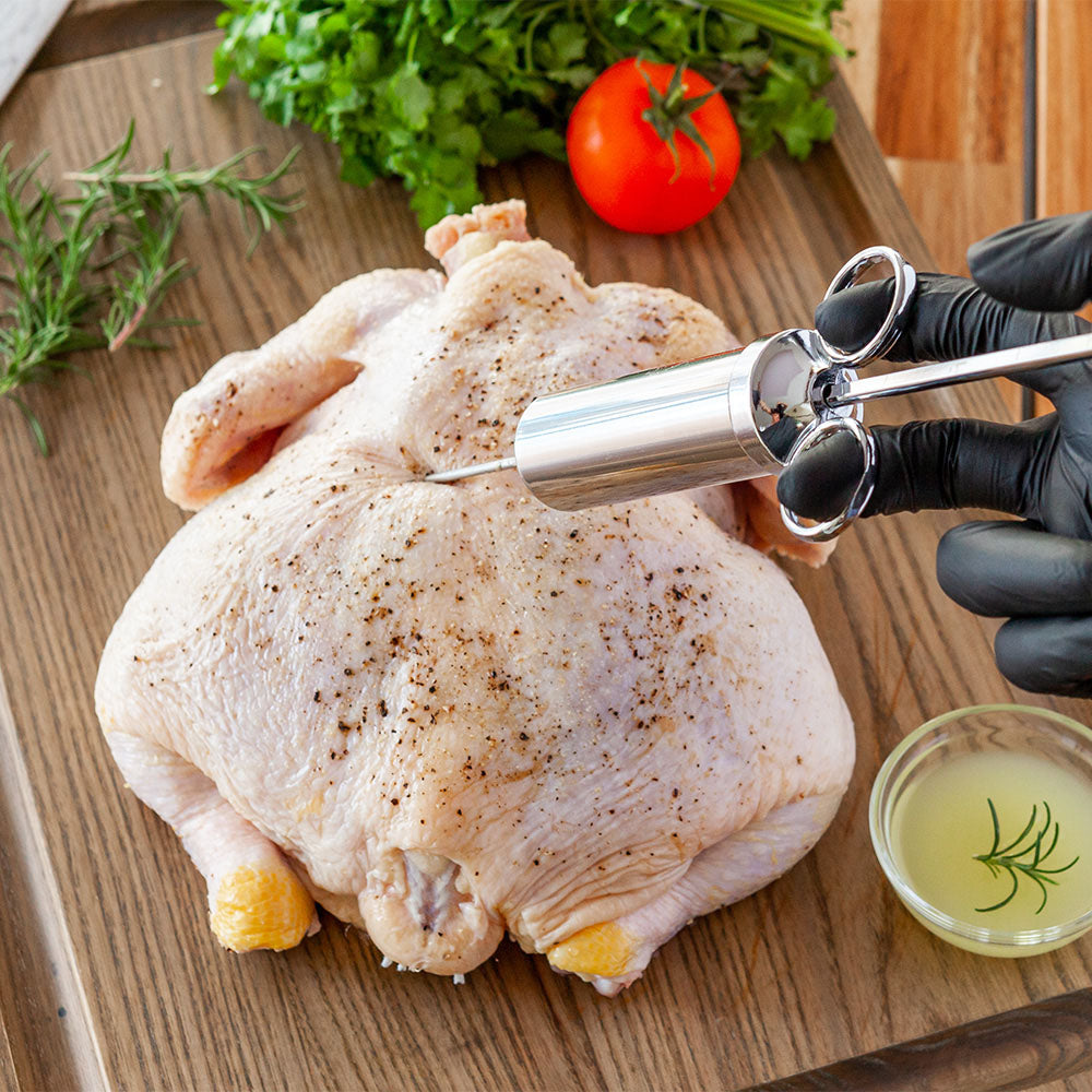 Meat injector tool injecting chicken on wooden board with marinade cup