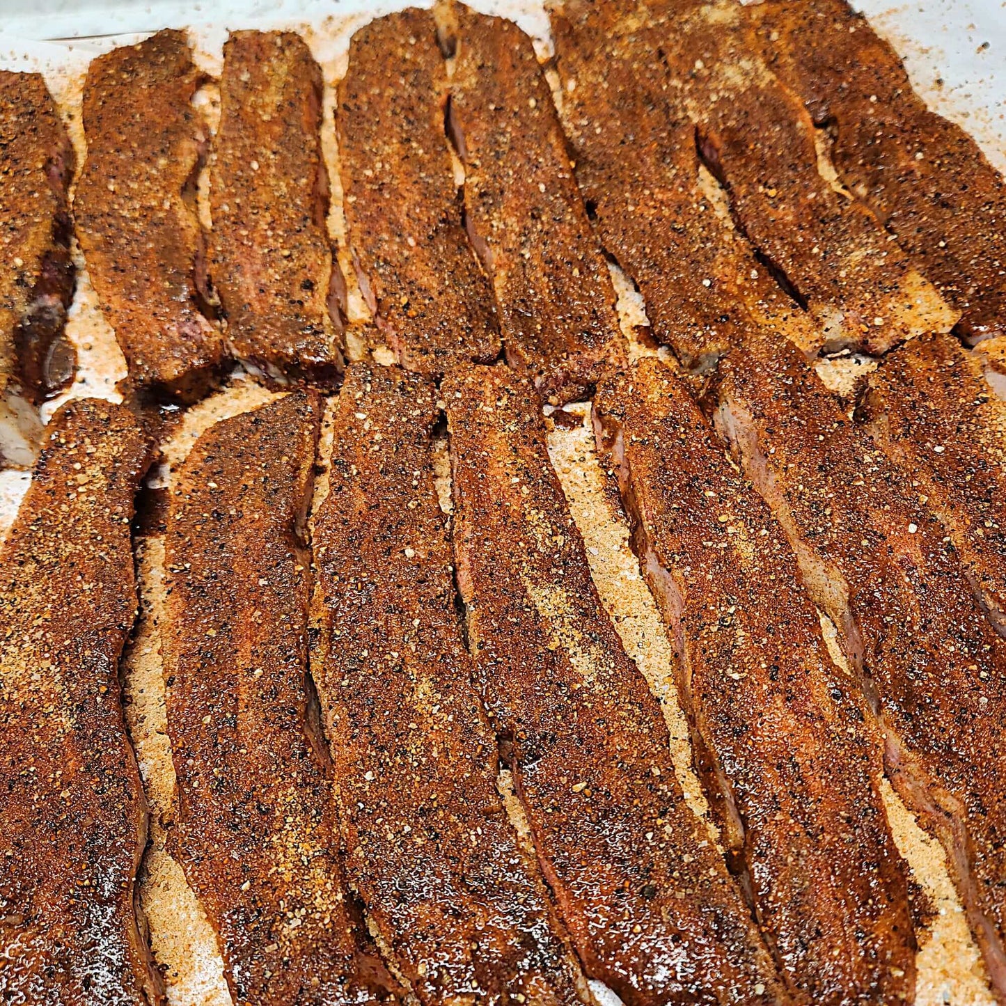 Seasoned beef rub coating with gritty spice texture on meat strips