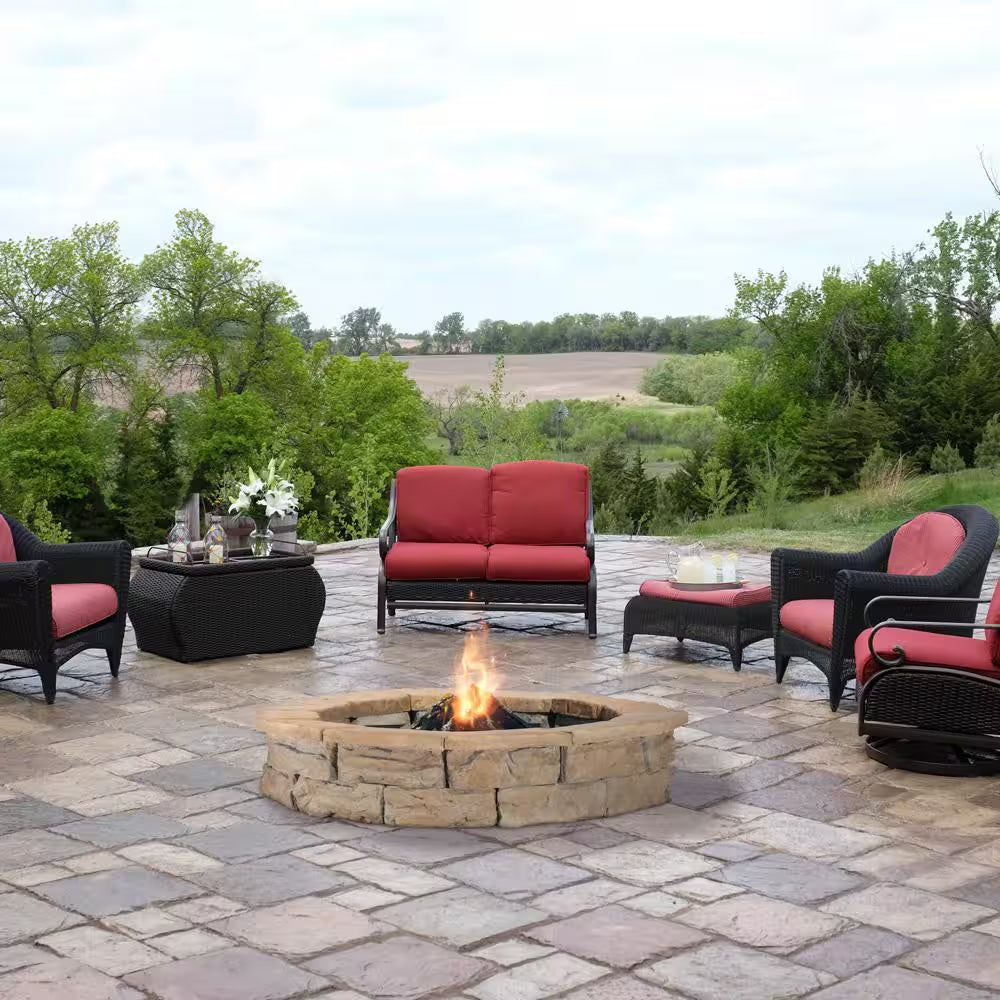 Round stone fire pit with visible flame in dark metal bowl on outdoor patio