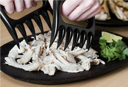Black bear-claw meat shredder shredding white meat with long prongs on a platter