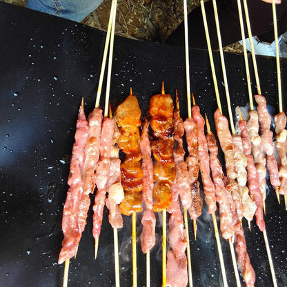 Black non-stick grill mat with rows of grilled meat on skewers