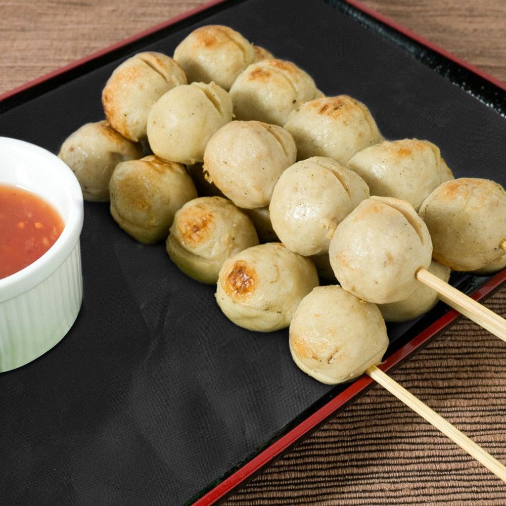 Black non-stick grill mat with small grilled bites and dipping sauce