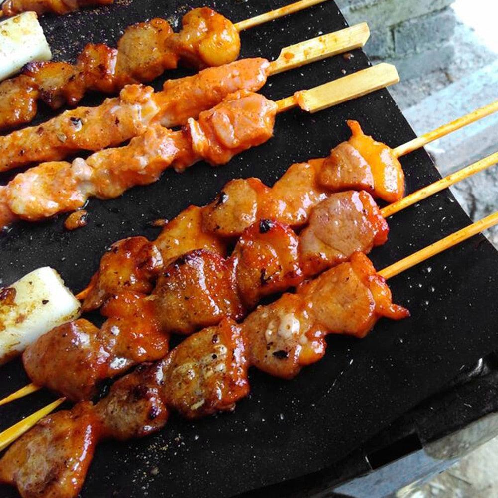 Black non-stick grill mat with grilled skewers and browned meat pieces