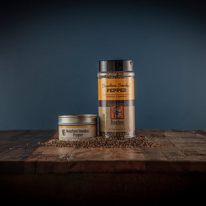 Smoked pepper seasoning jar and tin with coarse pepper on a wooden board