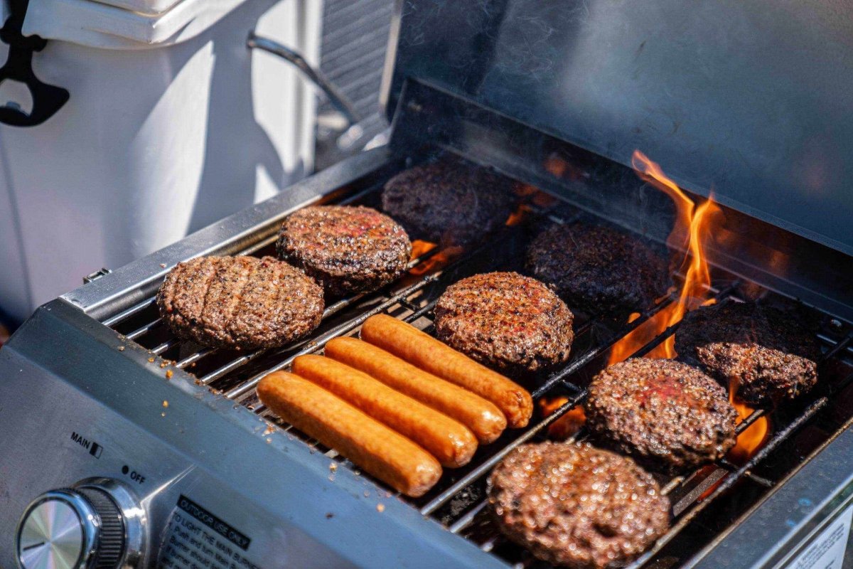 Stainless tabletop propane gas grill cooking burgers and hot dogs with flames