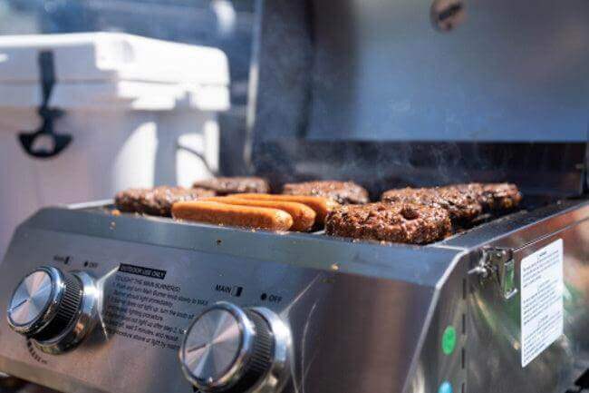 Stainless tabletop propane gas grill with searing burgers on grill grates