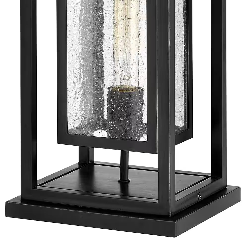 Black outdoor wall lantern with clear glass panel and warm bulb in center