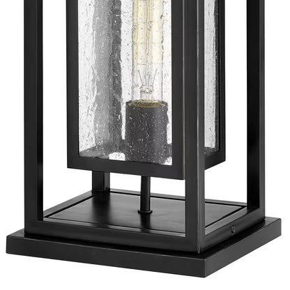 Black outdoor wall lantern with clear glass panel and warm bulb in center