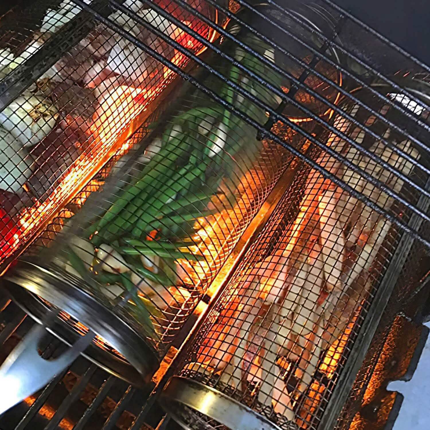 Round mesh BBQ baskets filled with vegetables and meat over open flames