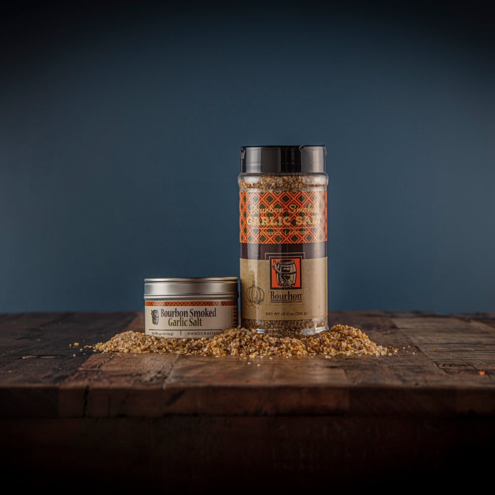 Two smoked garlic salt jars and a pile of coarse seasoning on a wooden surface