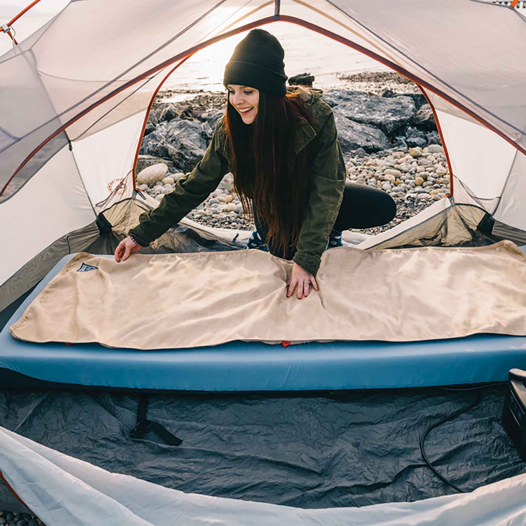 Heated bed cover laid on outdoor mattress inside a tent for camping warmth