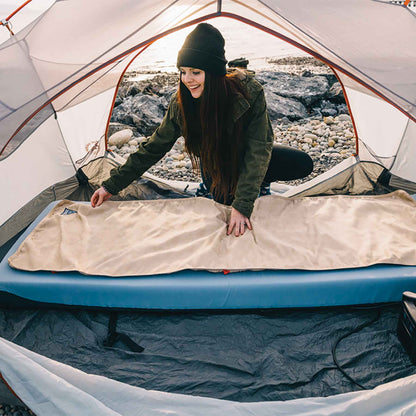 Heated bed cover laid on outdoor mattress inside a tent for camping warmth