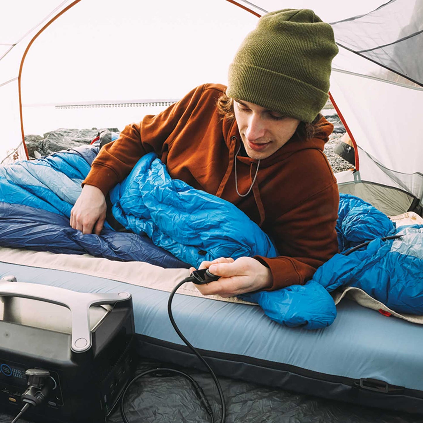 Heated bed cover in use in a tent, with a corded controller powering the heat