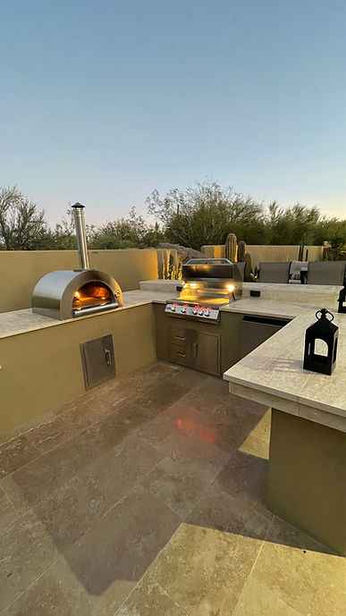 Built-in outdoor wood-fired pizza oven with open dome mouth and tall chimney