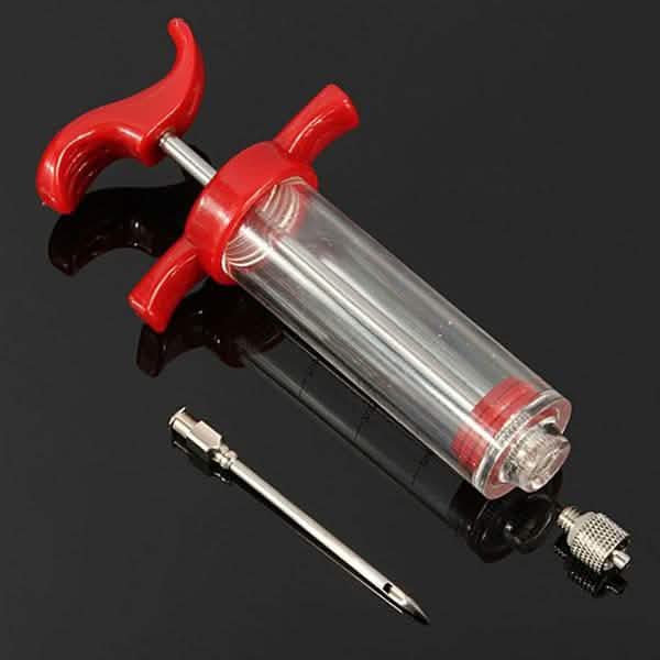 Marinade injector syringe with red levers, clear barrel and long metal needle