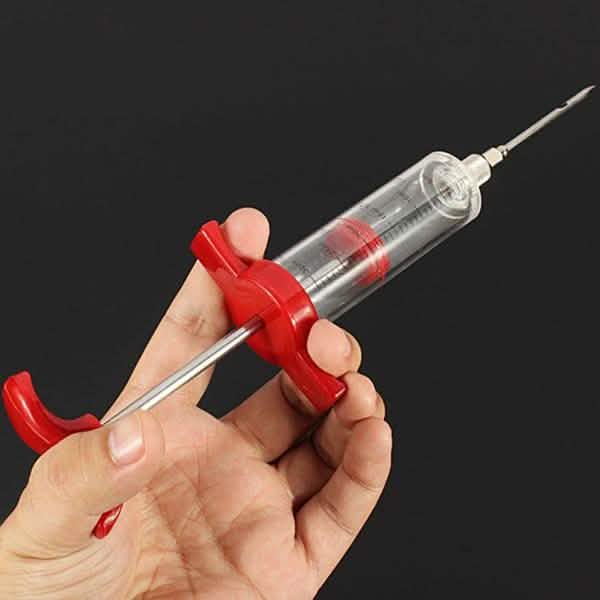 Hand holding marinade injector syringe with red grips, clear barrel and needle tip