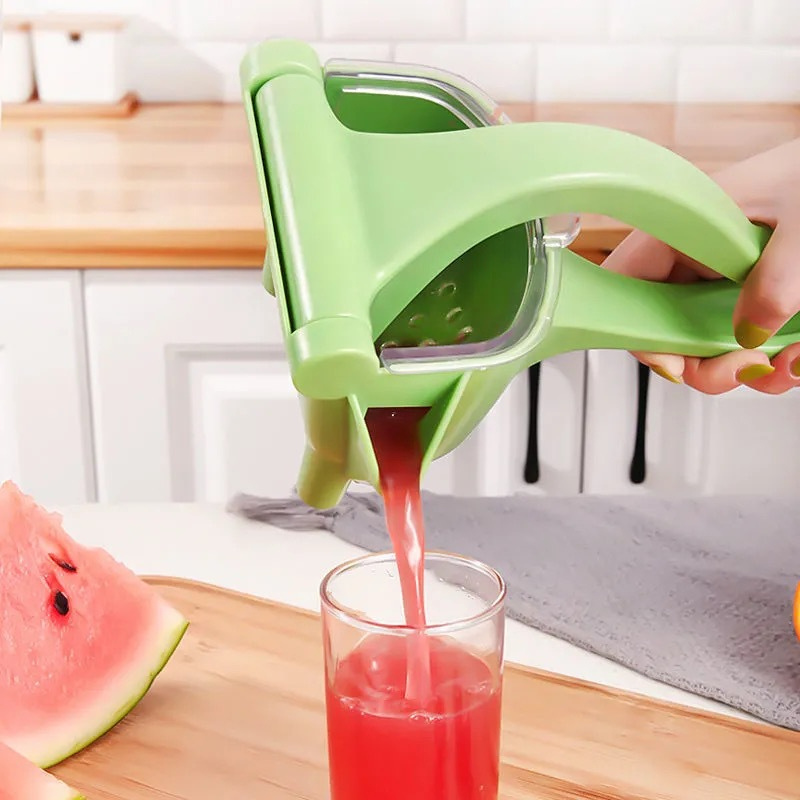 Green hand citrus juicer squeezing red juice into a clear cup