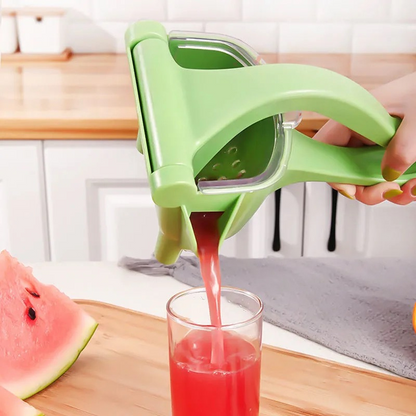 Green hand citrus juicer squeezing red juice into a clear cup