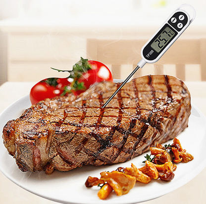 Digital BBQ thermometer with probe in a cooked steak, on a plate