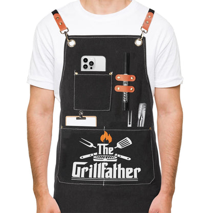 Men's black canvas chef apron with front chest pocket, grilling utensils graphic and straps