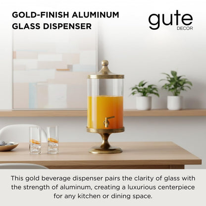Gold beverage dispenser with clear glass cylinder and gold spigot, holding orange drink