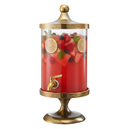 Gold beverage dispenser with clear glass cylinder, gold spigot, and red fruit drink