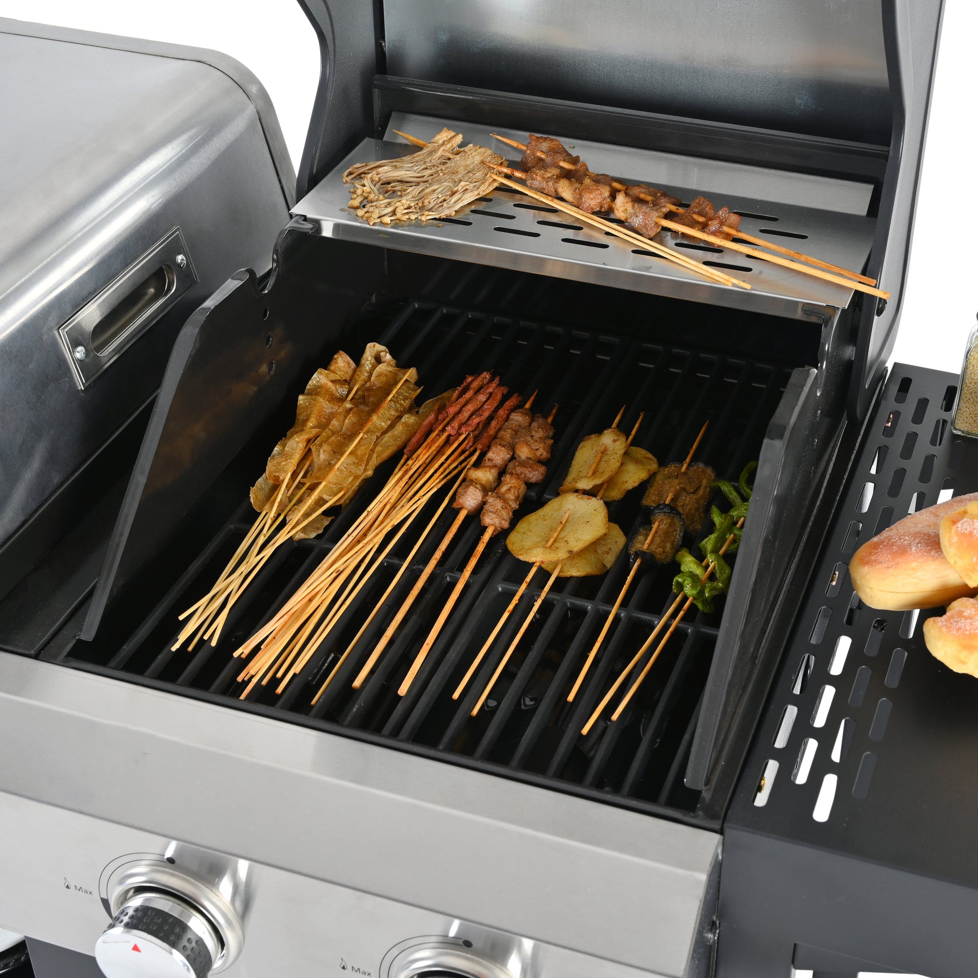 Open gas grill with cooking grates holding skewers and vegetables