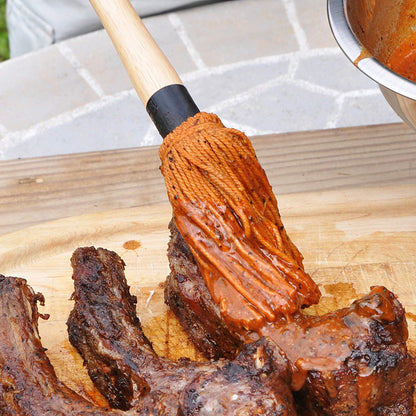 Cotton grilling mop applying oil to steak on a wooden board