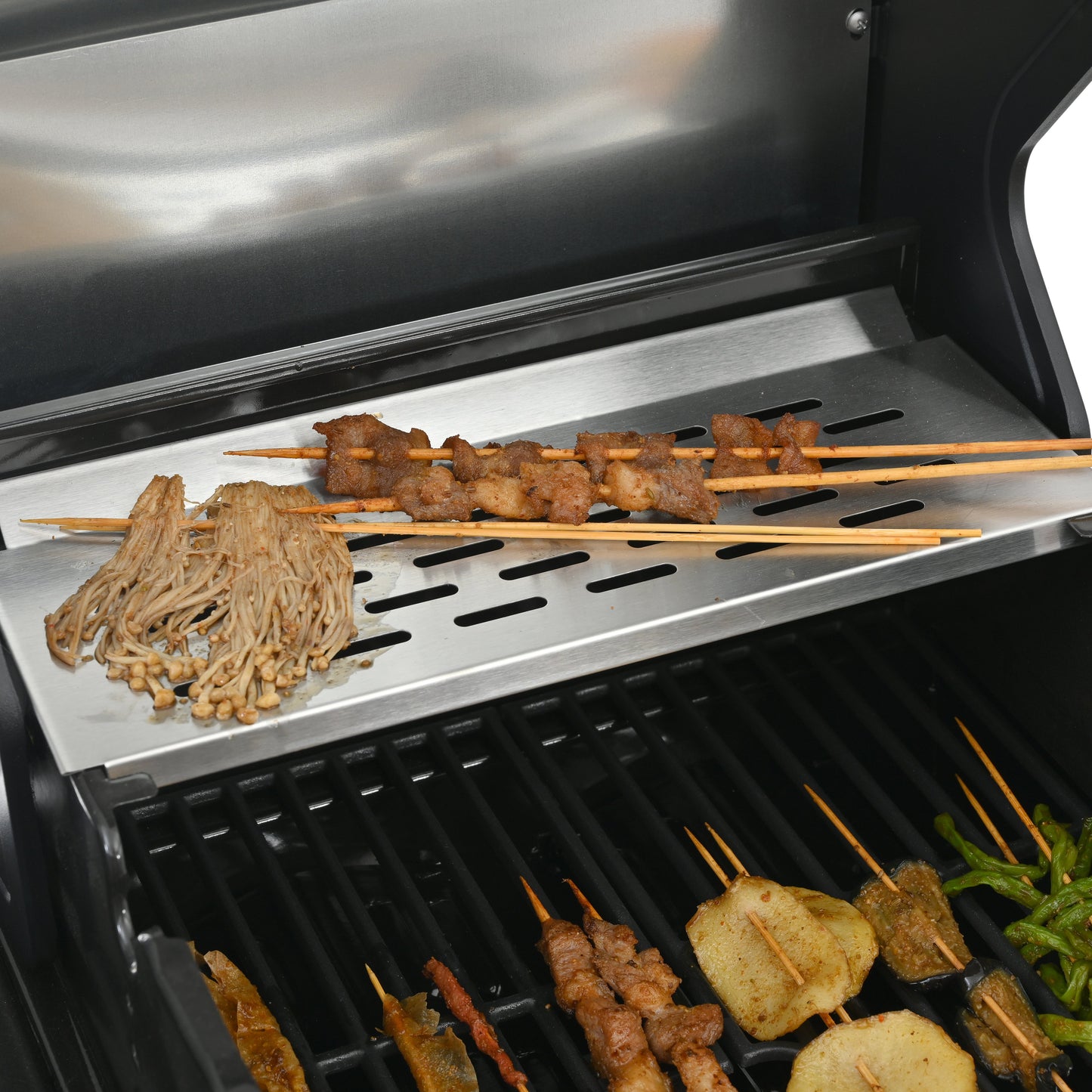 Griddle cooking surface with sliced meat, vegetables, and skewers over burner grates