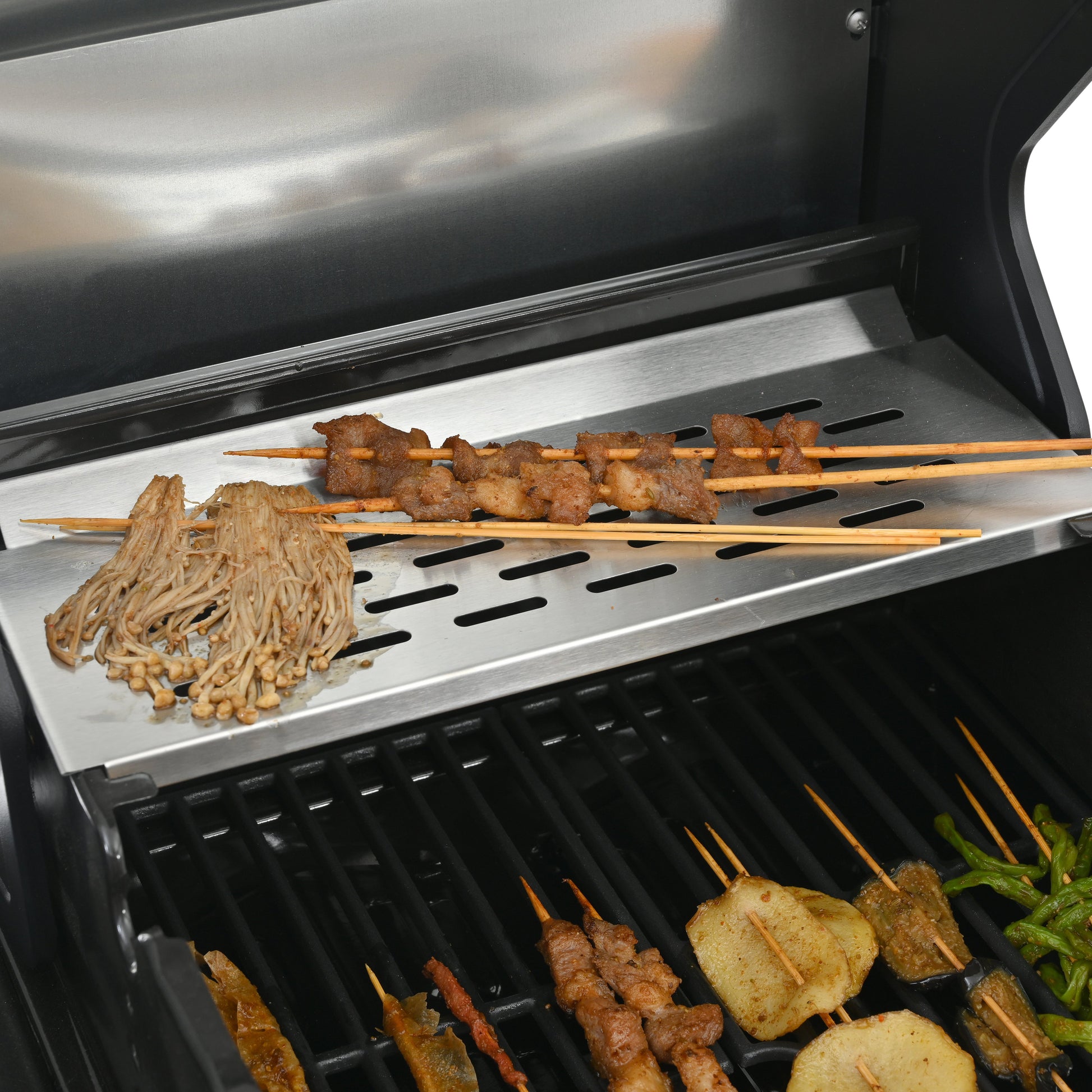 Griddle cooking surface with sliced meat, vegetables, and skewers over burner grates