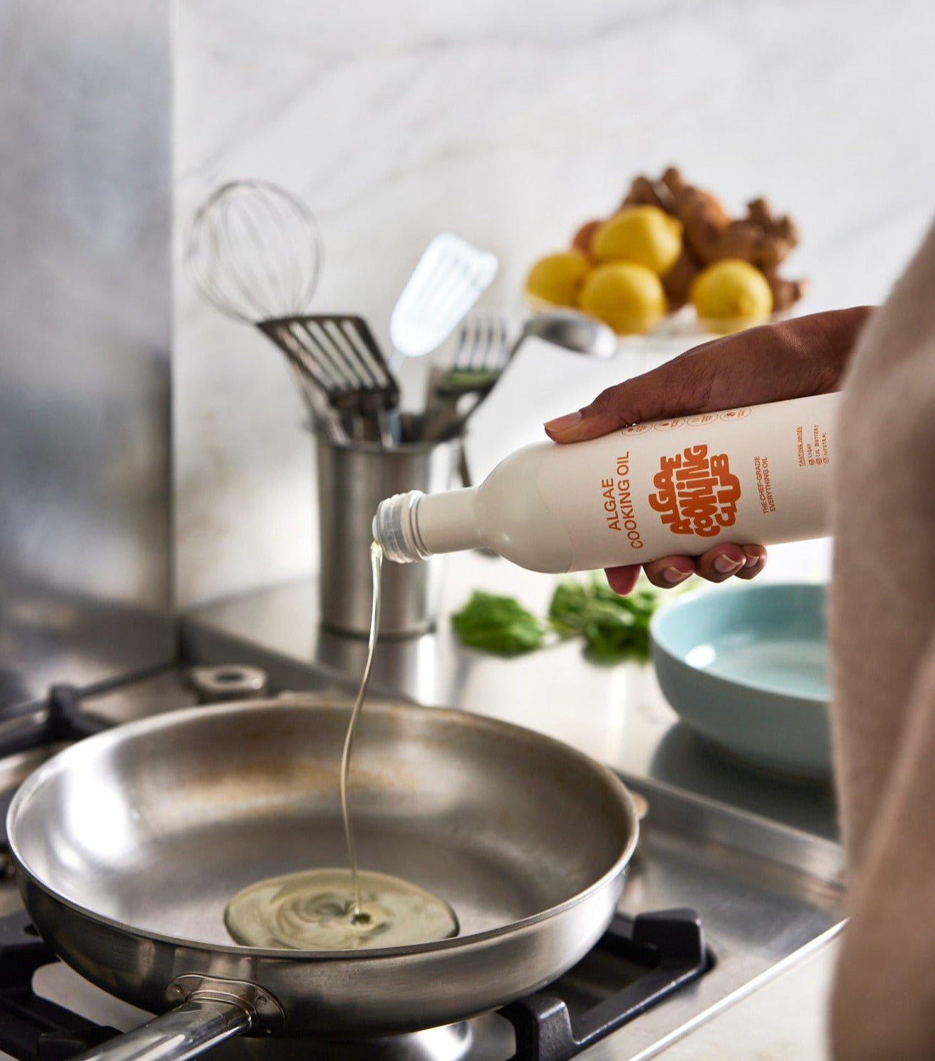 Hand pouring algae cooking oil from bottle into a skillet