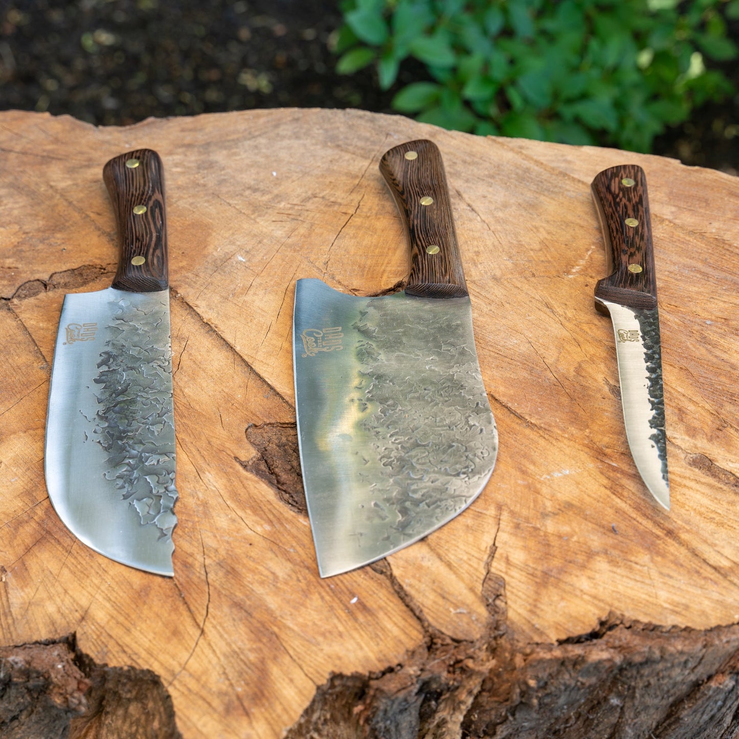 Three stainless hammered cleaver knives with dark wood handles on a wooden cutting board
