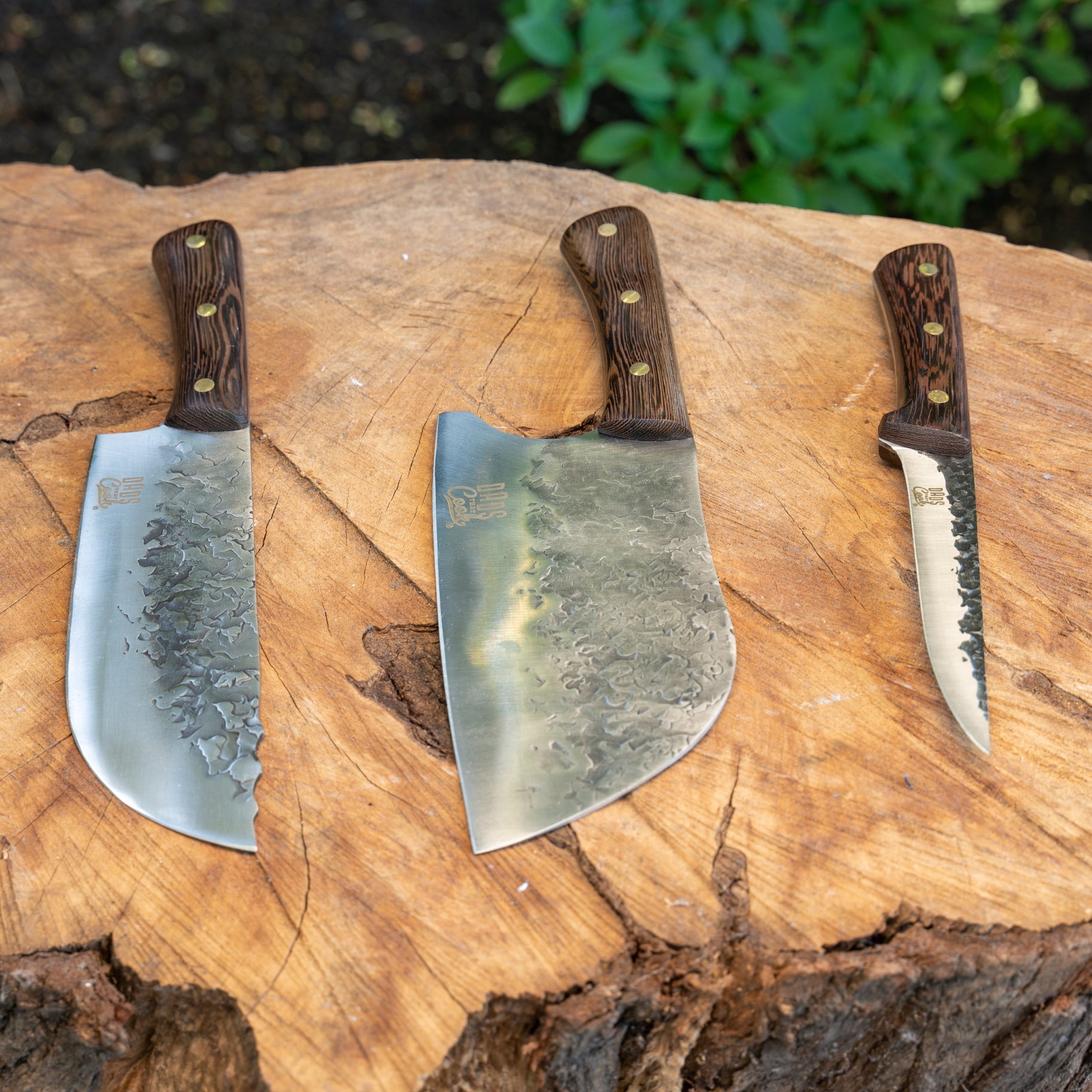 Three stainless hammered cleaver knives with dark wood handles on a wooden cutting board