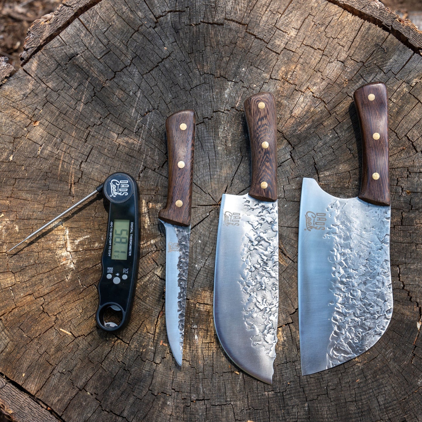 BBQ knife set on a log with two cleavers, a boning knife, and a digital thermometer