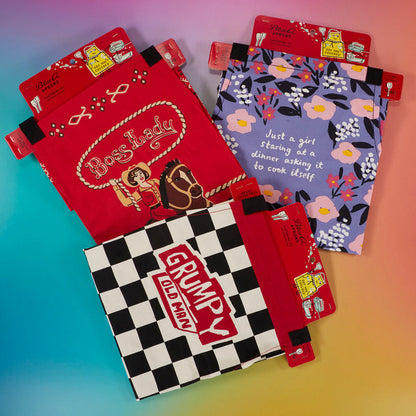 Red Boss Lady BBQ apron in packaging, hang tags attached, shown with other printed aprons