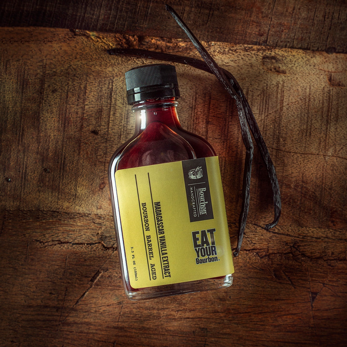 Vanilla extract bottle with dark cap, amber-burgundy liquid, and vanilla bean pod