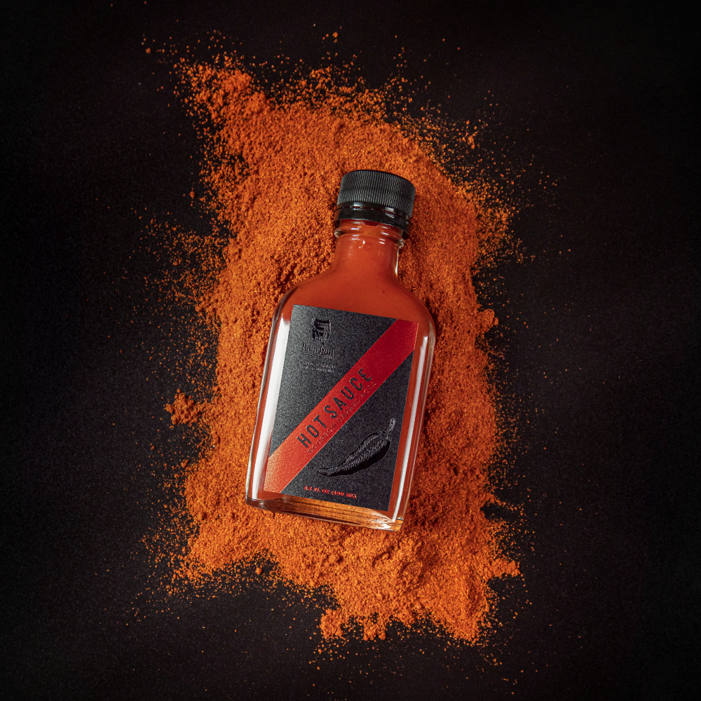 Hot sauce bottle with black cap and red-orange spice powder splash