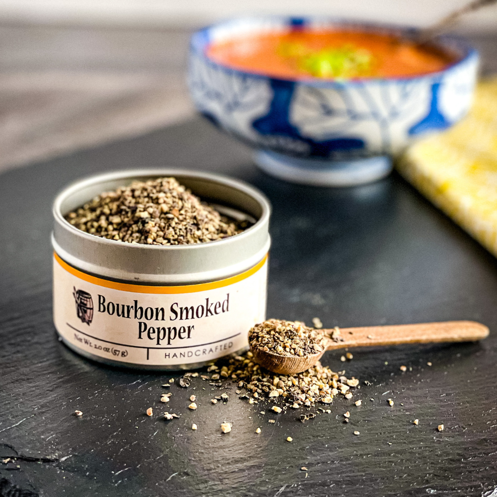 Smoked pepper seasoning jar with spoon and coarse pepper flakes on dark surface