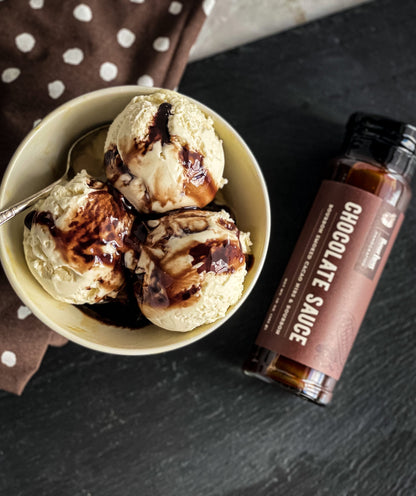 Chocolate sauce bottle with ice cream topped with chocolate drizzle and cacao nibs