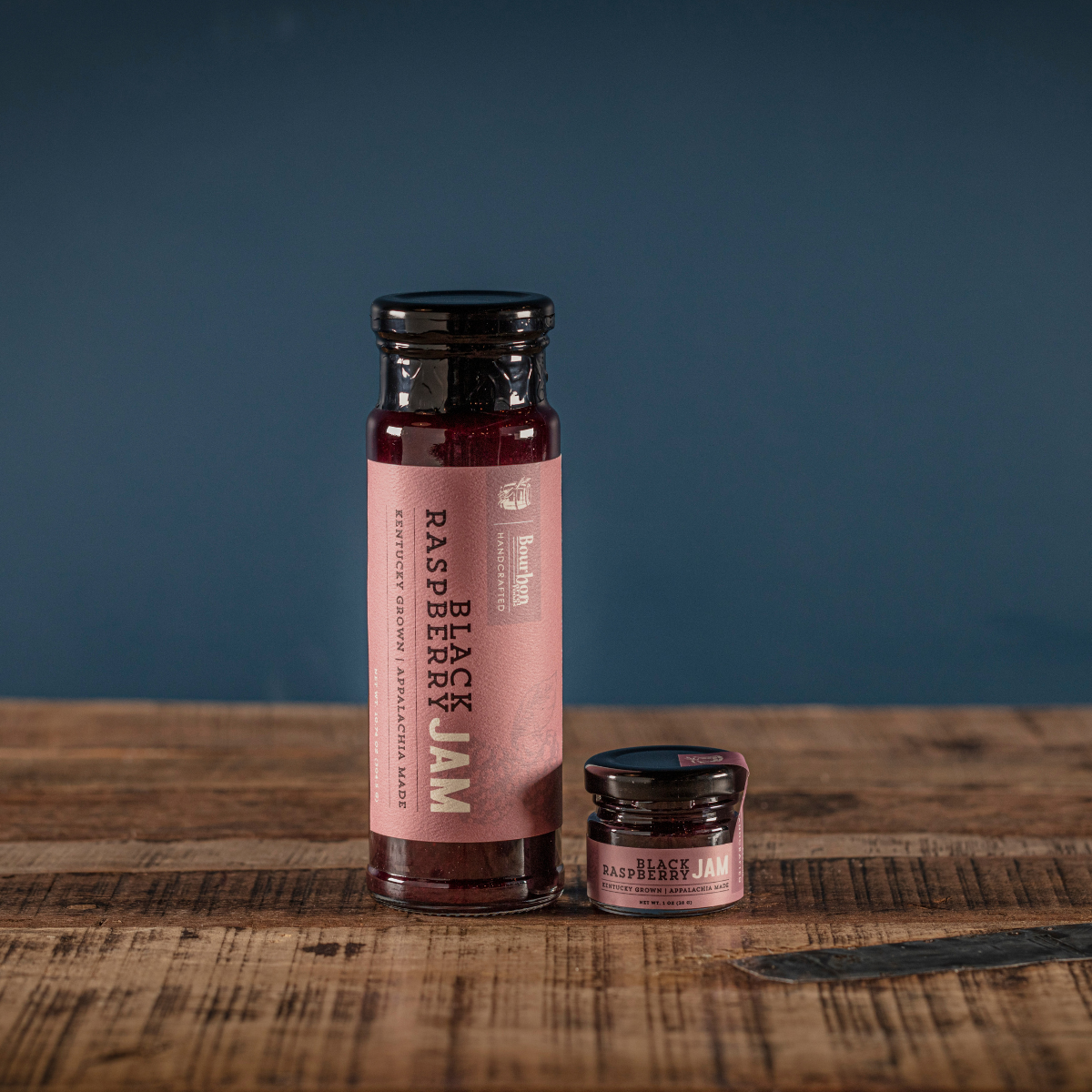Black raspberry jam bottle with small jar on a wooden board