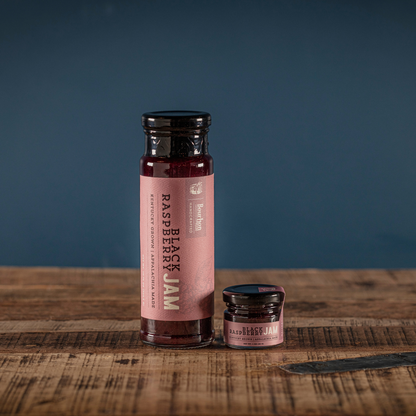 Black raspberry jam bottle with small jar on a wooden board