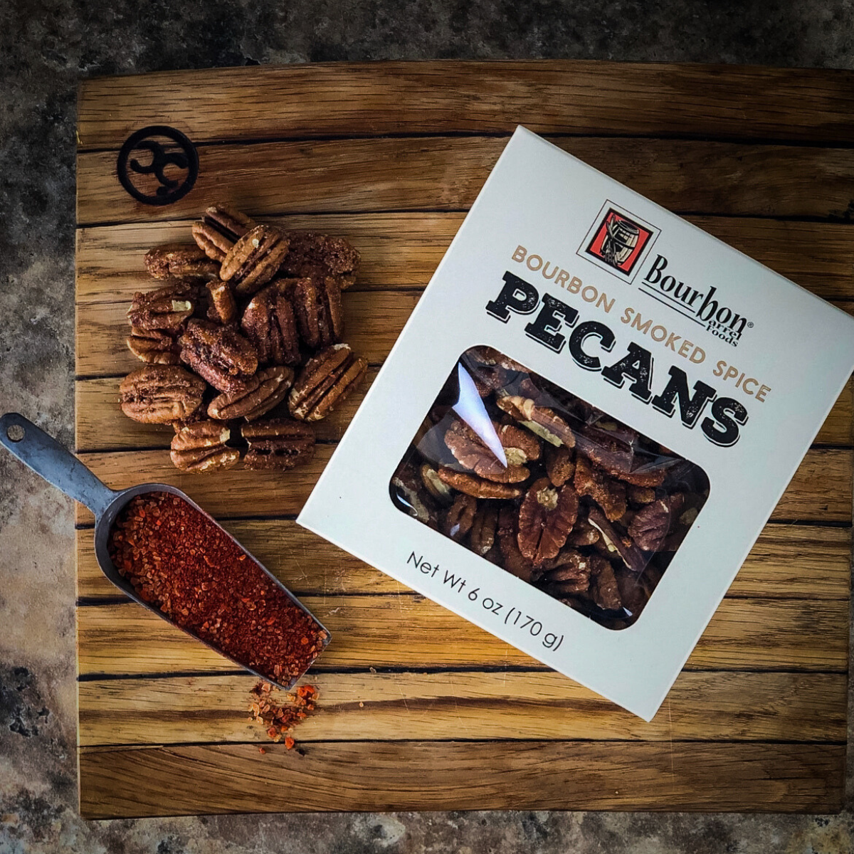Bourbon smoked spice pecans on wooden board with spoon and product box