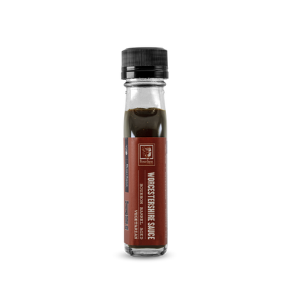 Worcestershire sauce bottle with amber-brown liquid and black ribbed cap, side label view