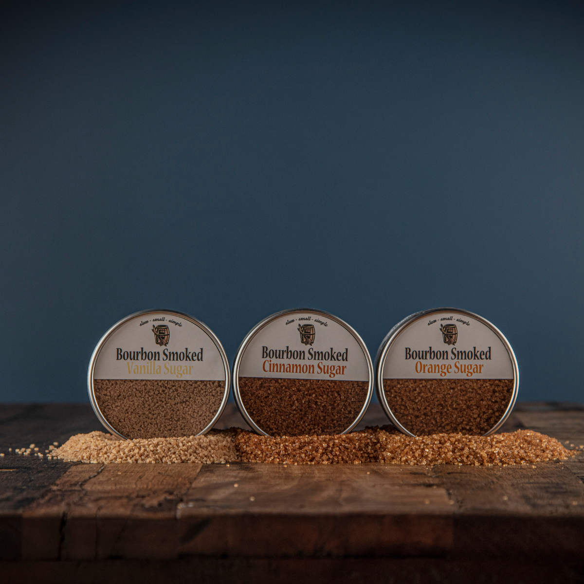 Three round tins of bourbon smoked sugar labeled vanilla, cinnamon, and orange