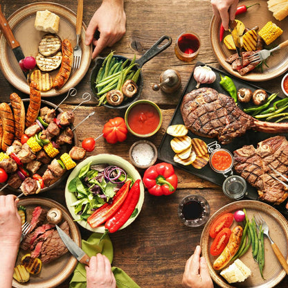 Mixed grilled meal spread on a wooden table with vegetables, bread, and steak