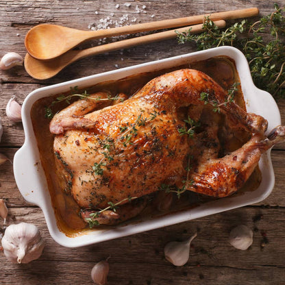 Seasoned whole chicken in a baking dish with herbs, garlic, and salt on top