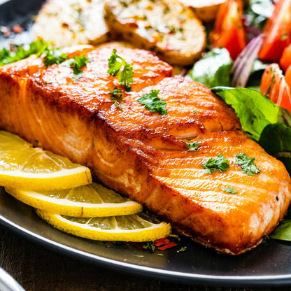 Sliced seasoned salmon on a tray with lemon wedges and herbs