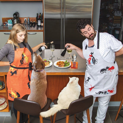 White cat apron on person serving food; cat print and “CATS” logo on front